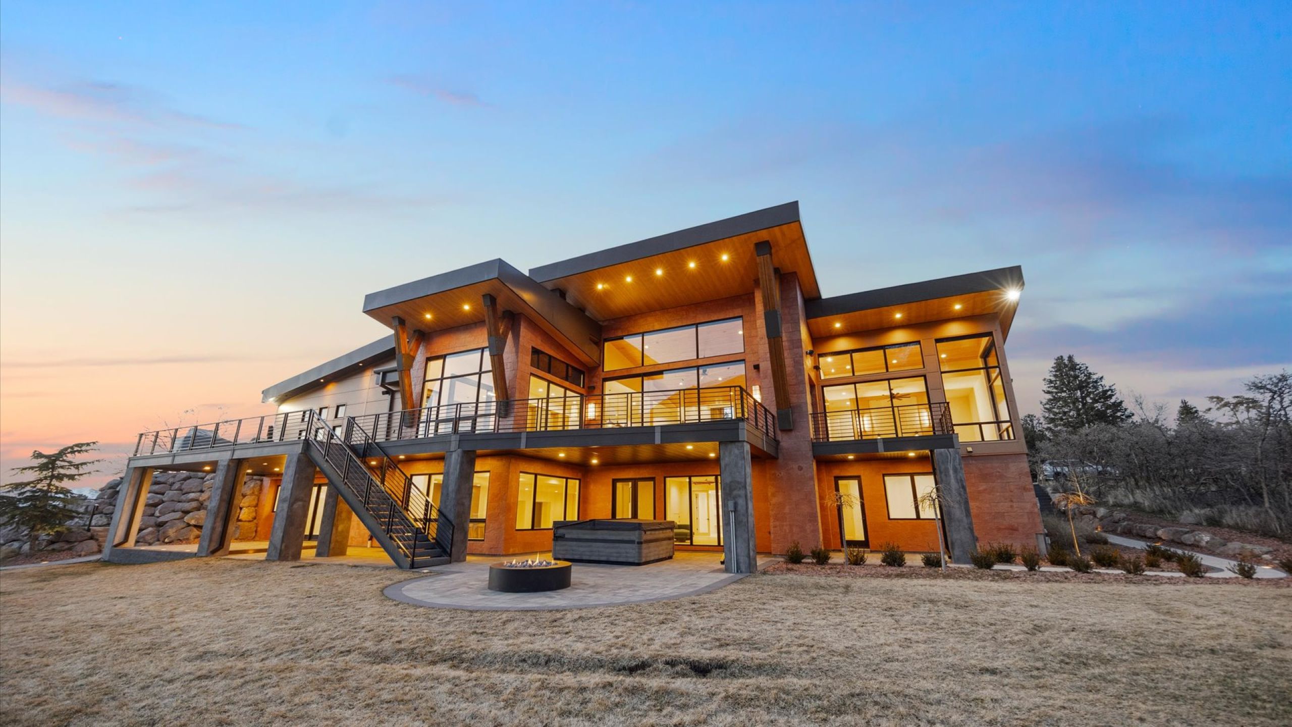 Rear view of property featuring a patio, a balcony, a lawn, and a fire pit